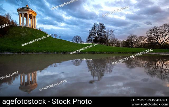 30 March 2023, Bavaria, Munich: The Monopteros is reflected in a puddle in the English Garden at sunset. The German Weather Service forecasts cloudy and rainy...