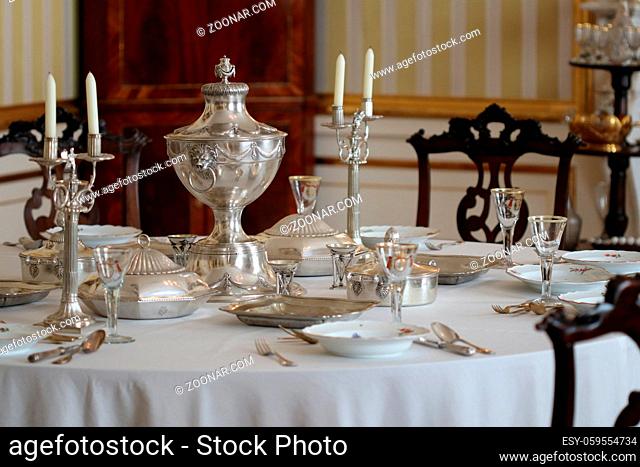Old vintage silver tableware set out on table with white tablecloth in vintage interior