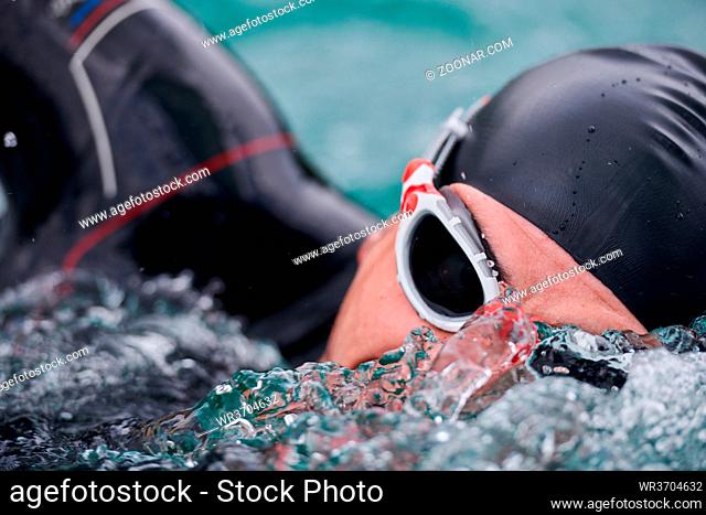 triathlon athlete swimming on extreme morning training in green lake wearing wetsuit