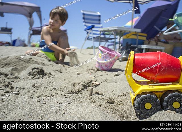 Little boy playing with sand and beach toys. Beach site full of beach furniture