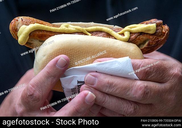 05 August 2021, Saxony, Aue-Bad Schlema: A man holds a bratwurst after being vaccinated against the coronavirus. For the two-day vaccination campaign
