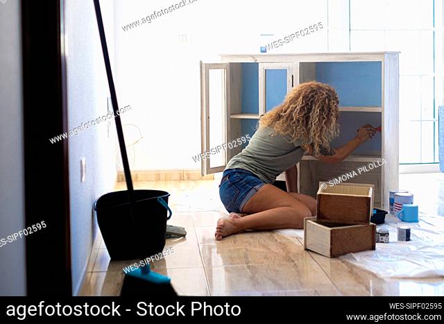 Mature woman painting cabinet at home