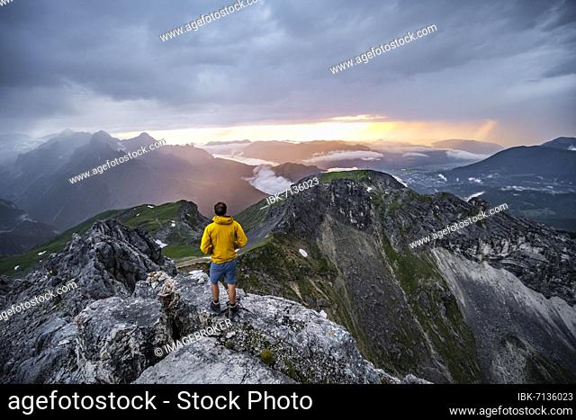 Hikers at the summit of the Westliche Törlspitze, in the background cloudy mountains at sunset with dramatic light, view of Frauenalpl, Wetterstein Mountains