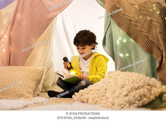 happy boy reading book in kids tent at home