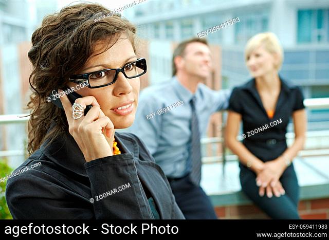 Business people talking on terrace outdoor of office building. Businesswoman in front using mobile phone