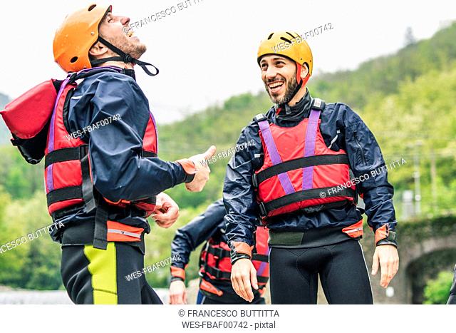 Laughing friends in protective wear at river shore
