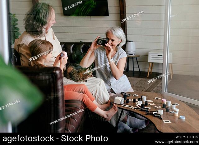 Woman taking photo of senior man and granddaughter on vintage film camera at home