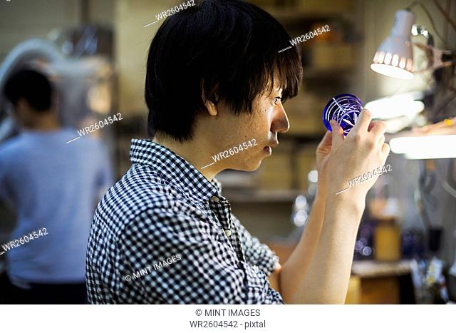 A craftsman at work in a glass maker's workshop working on a vivid blue cut glass object