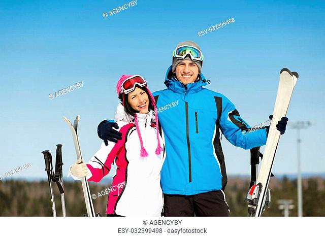 Half-length portrait of two embracing downhill skiers with skis in hands