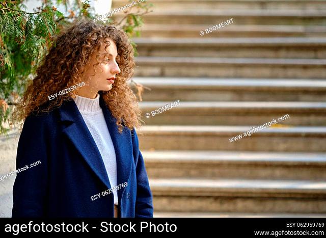 Young woman in blue coat stands in profile with the staircase on background