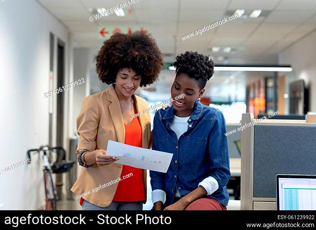 Smiling hispanic and african american businesswomen discussing over document at modern workplace