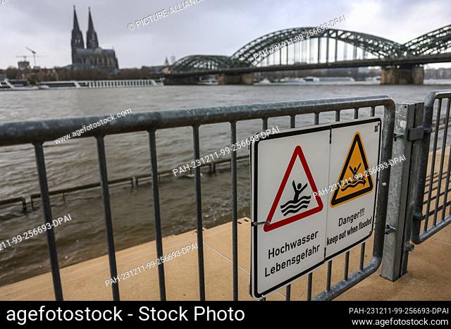 11 December 2023, North Rhine-Westphalia, Cologne: Signs with the words ""Flood - danger to life"" hang on the cordoned-off flight of steps on the banks of the...