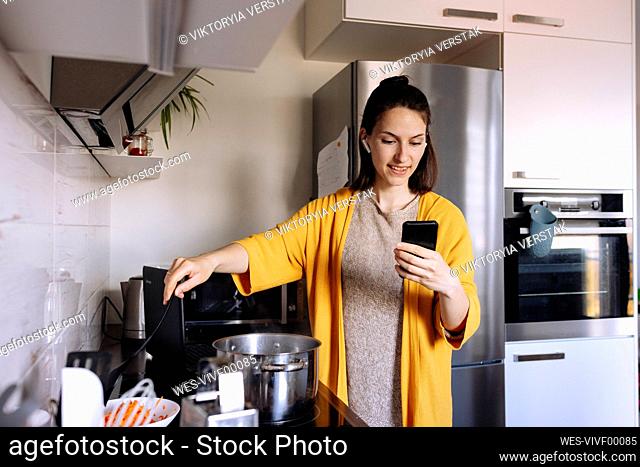 Woman cooking and having video call through smart phone in kitchen