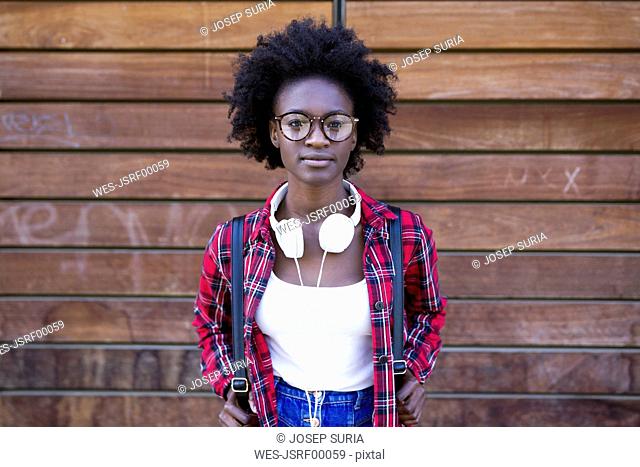Portrait of young woman with backpack and headphones in front of wooden wall