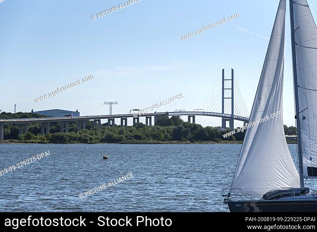 13 August 2020, Mecklenburg-Western Pomerania, Stralsund: A sailing boat is sailing on the Strelasund, an inlet of the Baltic Sea, past the Rügen Bridge