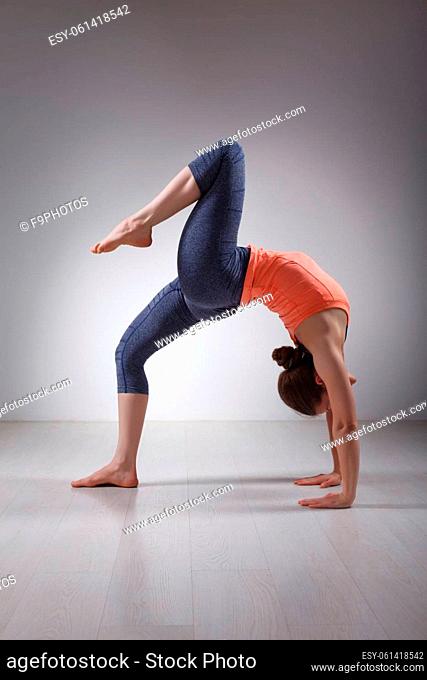 Beautiful sporty fit yogini woman practices yoga asana eka pada chakrasana (or eka pada urdva dhanurasana) - one-legged wheel pose (or one-legged upward facing...