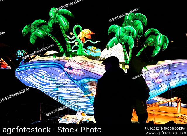 19 December 2023, Saxony-Anhalt, Halle (Saale): Visitors look at a giant illuminated whale. At Bergzoo Halle, the magical worlds of light whisk visitors away to...