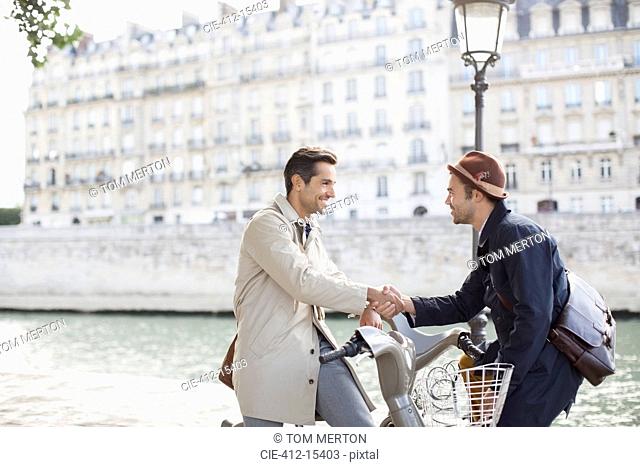Businessmen handshaking on bicycles along Seine River, Paris, France