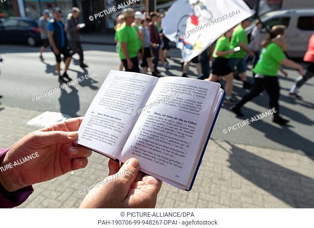 06 July 2019, Lower Saxony, Glandorf: Pilgrims of the Telgte pilgrimage walk on a road, in the foreground a song book. Around 40 kilometres of country road lie...