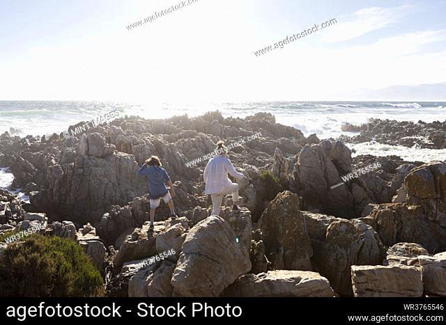 Two children exploring the jagged rocks and rock pools on the Atlantic Ocean coastline, De Kelders, Western Cape, South Africa