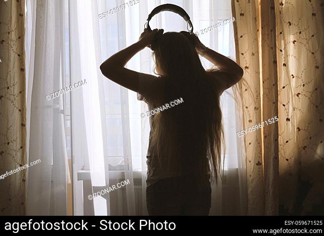 Silhouette of teenager girl wearing headphones in front of the window, concept of youth leisure