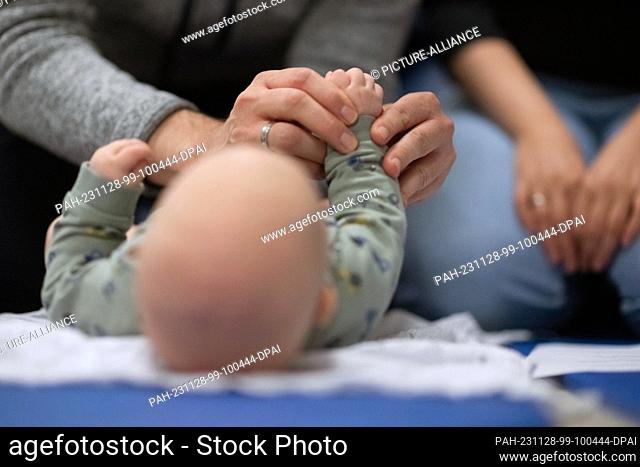 SYMBOL - 24 November 2023, Baden-Württemberg, Stuttgart: A father holds his child's feet during an infant handling course while the mother sits next to him