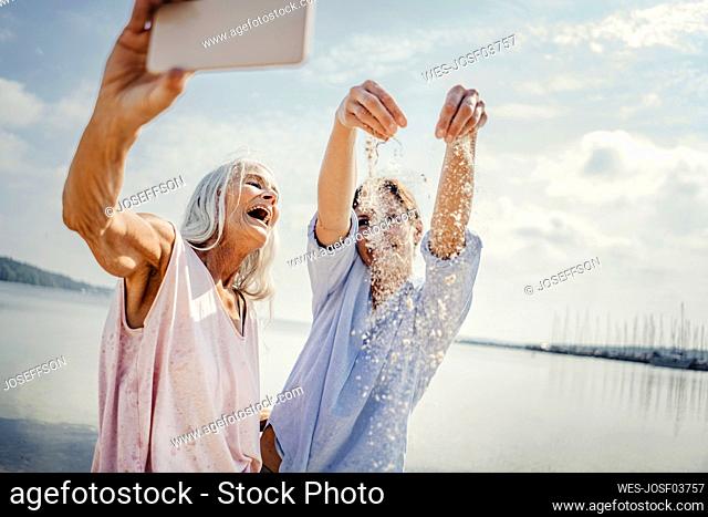 Mother and daughter havin fun on the beach, taking smartphone selfies
