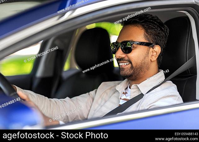 smiling indian man in sunglasses driving car