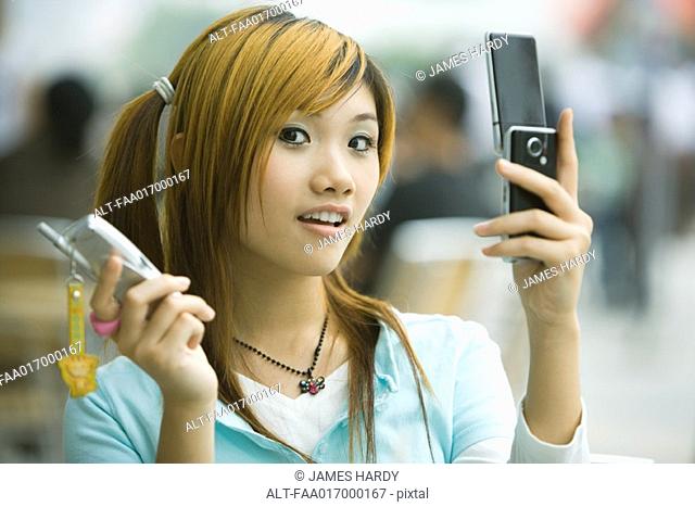 Young woman holding two cell phones, looking at camera