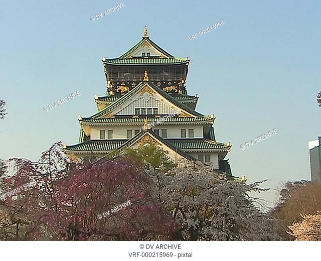 Worms-eye view of three-story green and gold Japanese temple surrounded by trees and other vegetation