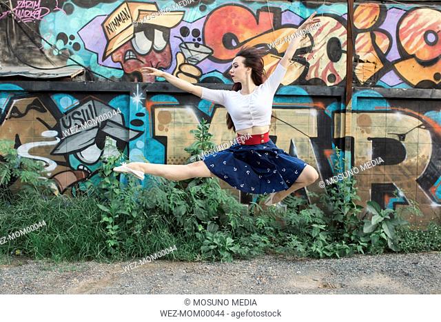 Ballerina jumping against graffiti wall