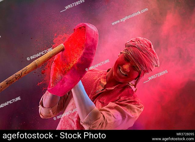 A HAPPY YOUNG MAN SHIELDING HIMSELF FROM STICK WHILE PLAYING HOLI