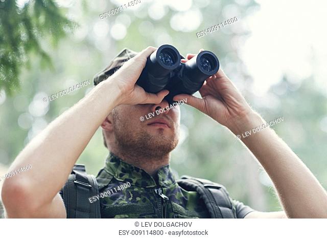 hunting, war, army and people concept - young soldier, ranger or hunter with binocular observing forest