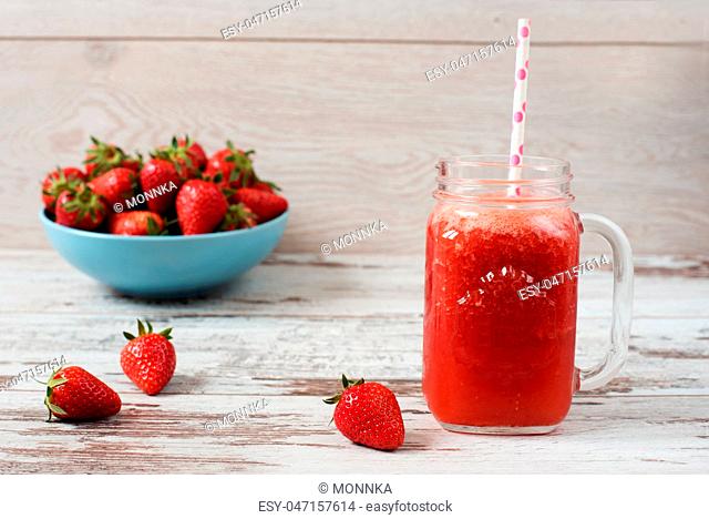 Fresh juice, shake, milkshake of strawberries in a mason jar with a straw. Pile of juicy ripe organic fresh strawberries in a large blue bowl