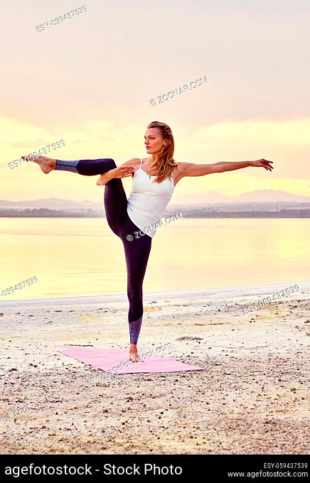 Yogi woman in activewear do balancing yoga pose, stand on one leg raising hand looking away practising exercise near salt lake on beautiful nature outdoors