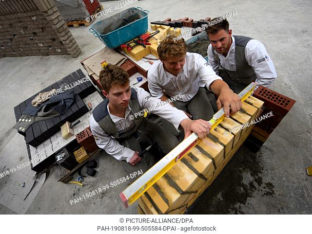 30 July 2019, Bavaria, Nördlingen: The bricklayers (l-r) Pierre Holze, Christoph Rapp and Jannes Wulfes inspect a wall in the training centre of the...