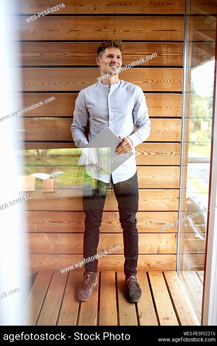Smiling man holding digital tablet while standing at home