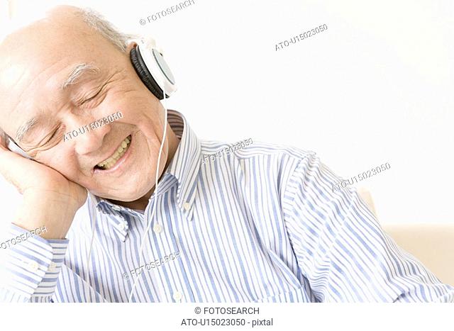 Senior man wearing a headphone, closing eyes, front view, white background