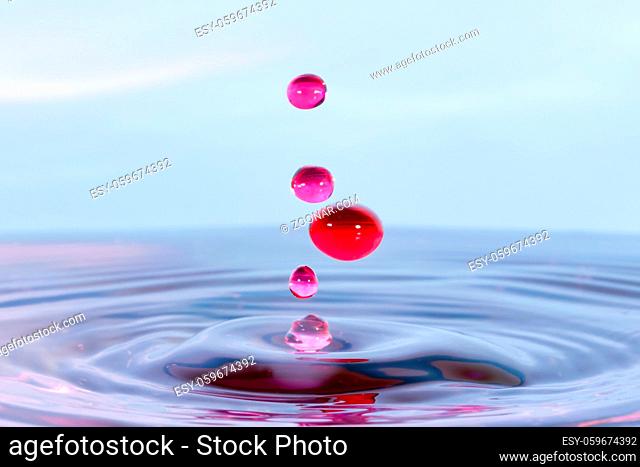 High speed water drop photograph with red colored falling drops against a blue background