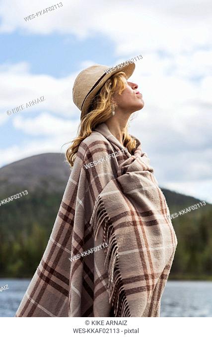 Finland, Lapland, woman wearing a hat wrapped in a blanket standing at the lakeside