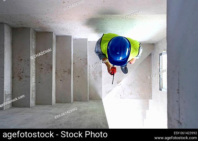 Engineer in hardhat, safety vest and Walkie-Talkie checking house structure while walking down a stairway. Day time work safety checks. Top View