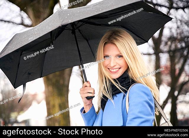 Portrait of smiling blond woman holding umbrella outdoors
