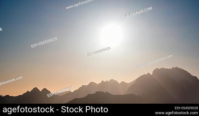 Sun glow in evening misty sky view. Mountain tops silhouettes in clouds. Climate, environment and weather concept sky background