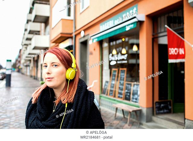 Young woman listening music through headphones outside cafeteria