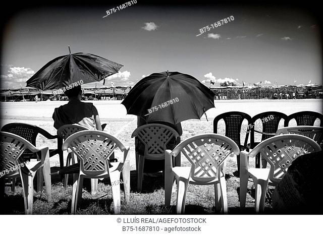 dos hombres de espaldas sentados, con paraguas, esperando en un campo de futbol, Campamento de refugiados Tibetano, India  Mundog, Two men sitting back