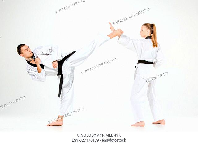 The karate girl and boy in white kimono and black belt training karate over gray background