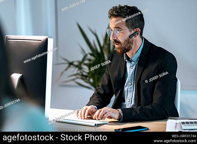 Businessman wearing bluetooth working on computer at office