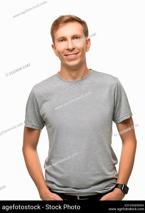 Young fair handsome male wearing gray t-shirt and jeans and keeping his hands in his pockets isolated portrait on white