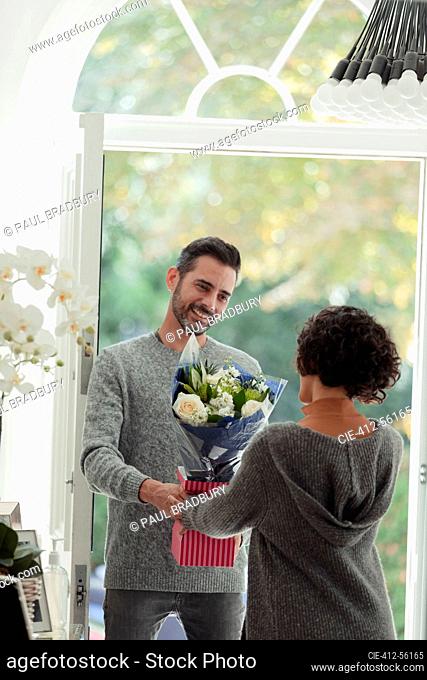 Happy husband surprising wife with flowers at front door