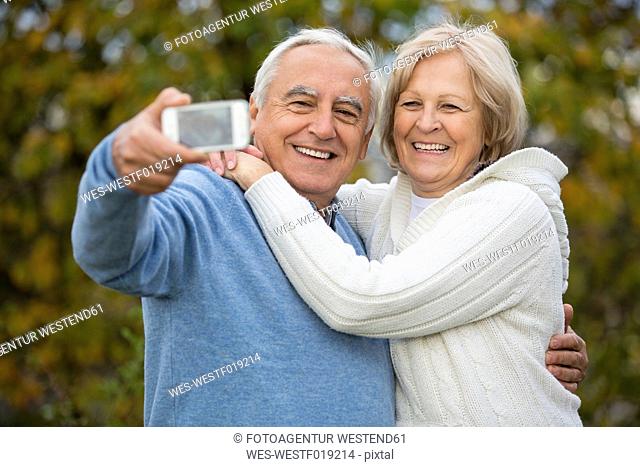 Portrait of smiling senior couple taking self-portrait with smartphone